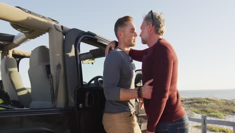 Glückliches-Kaukasisches-Schwules-Männliches-Paar,-Das-Am-Auto-Steht-Und-Sich-An-Einem-Sonnigen-Tag-Am-Strand-Umarmt