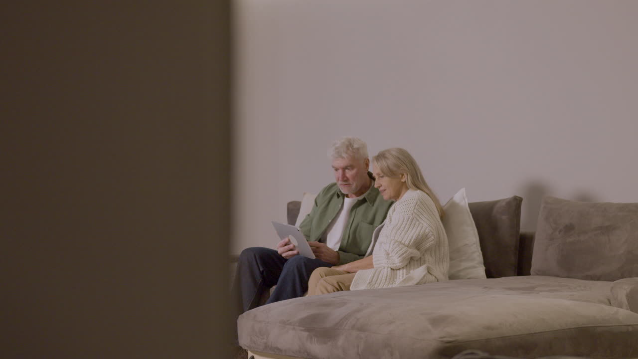 Senior Couple Sitting On Sofa At Home Using Digital Tablet