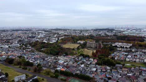 A-sprawling-cityscape-with-residential-areas-and-green-spaces-on-an-overcast-day,-crane-in-distance,-aerial-view