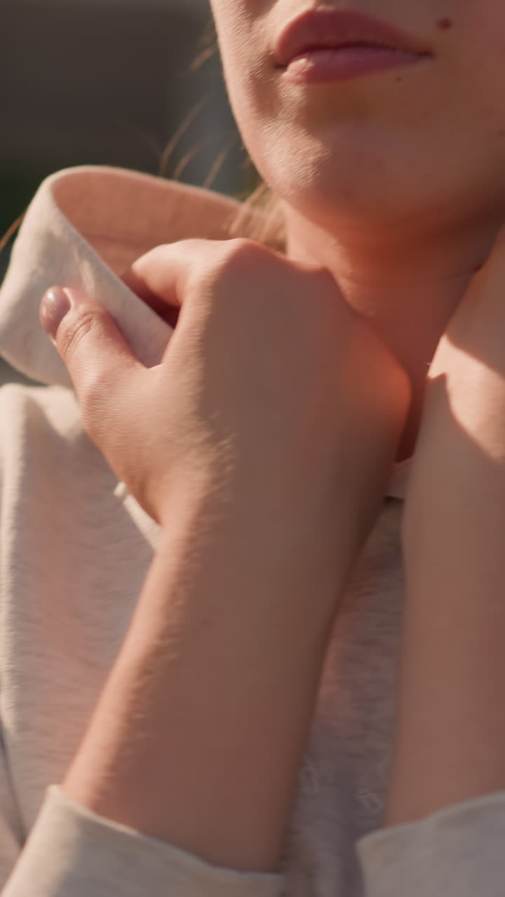 여성이 그녀의 후디 목걸이를 부드럽게 만지는 클로즈업, 손을 고 목에 고, 따뜻하고 반사적인 순간을 만들고, 부드러운 빛이 그녀의 피부와 캐주얼 옷을 강조합니다.