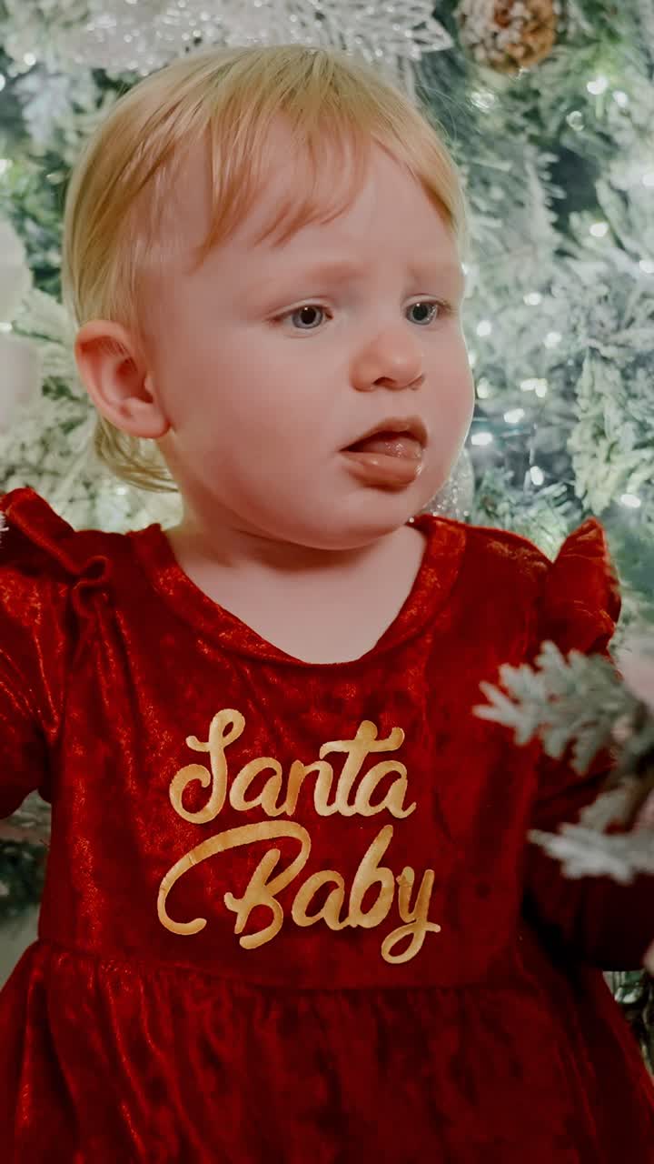 A Young Child in a Festive Red Dress with White Trim Sits Gracefully Amidst a Beautifully Decorated Christmas Tree, Radiating Joy and Holiday Spirit as the Lights Sparkle Around Her