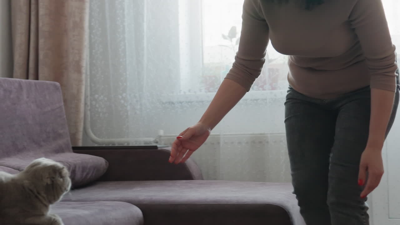 White Woman Prepares To Leave Beside Sofa And Orange Bag Thoughtful Movement Packing Small Items, Adjusting Strap, Looking Toward Window And Plants, Transitional Domestic Scene With Soft Light