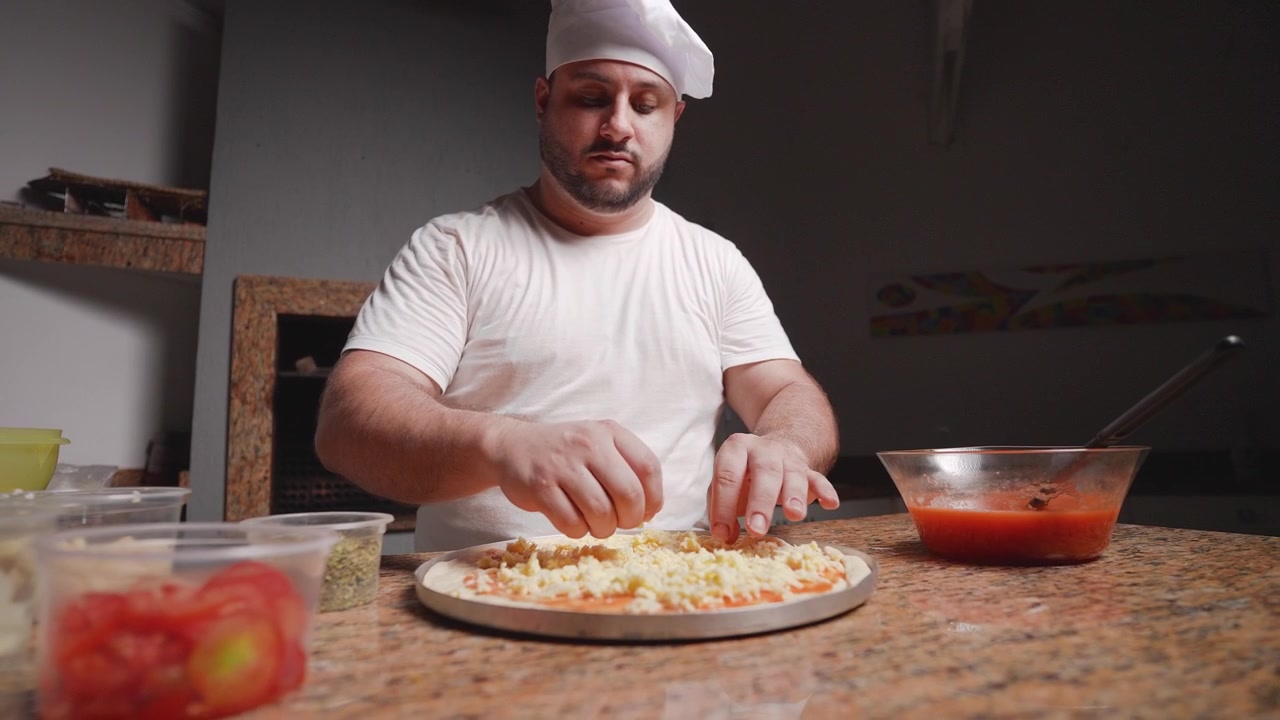 Uno chef professionista cosparge mozzarella fresca grattugiata su una base di impasto per pizza generosamente coperta di salsa di pomodoro