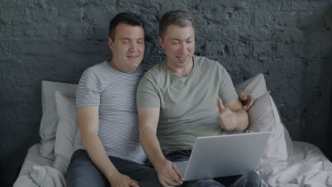 two men using laptop together in bed