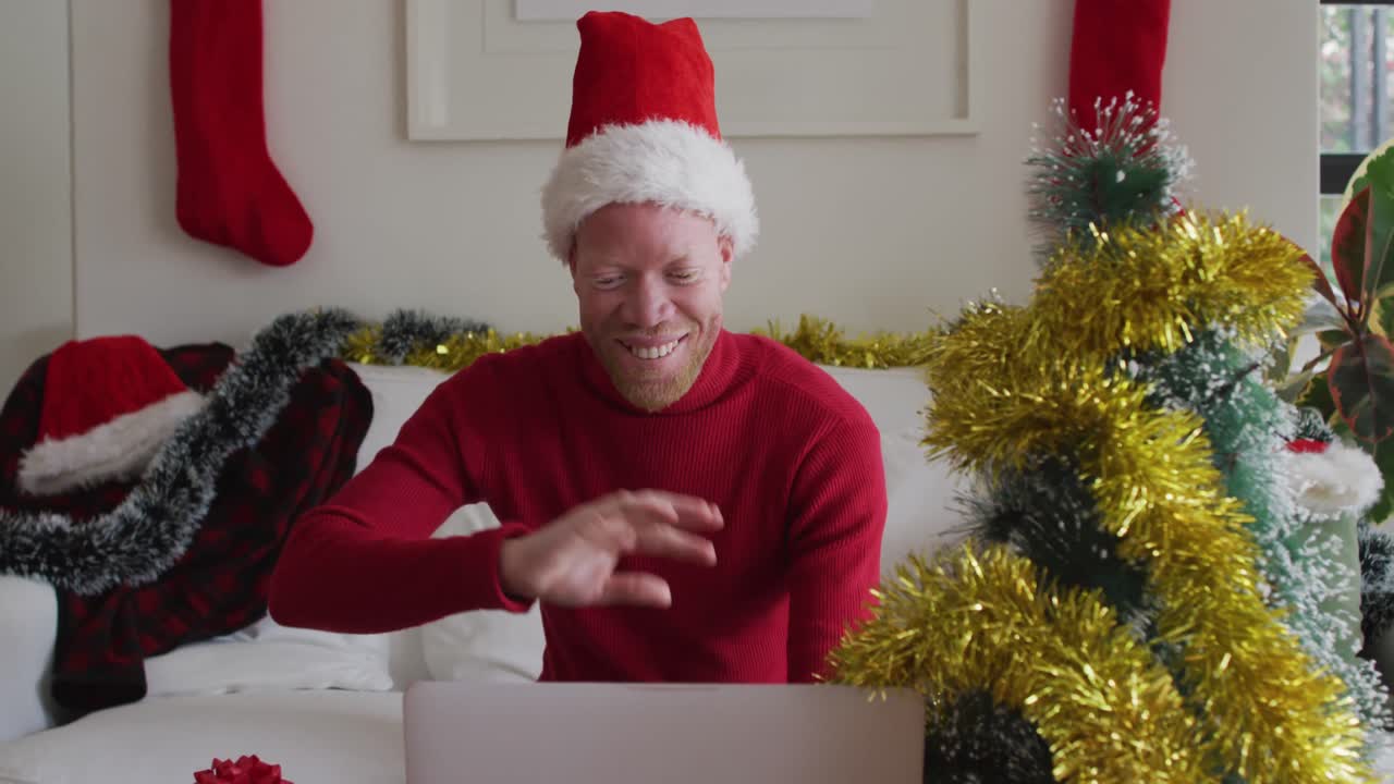 hombre afroamericano albino feliz con sombrero de papá noel haciendo una videollamada en navidad