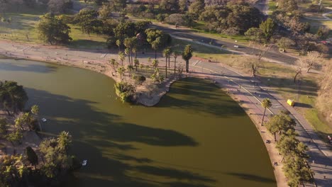 Toma-Aérea-De-Un-Hermoso-Lago-Natural-En-Buenos-Aires-Y-Mucha-Gente-Haciendo-Actividad-Deportiva-Y-Caminando---Vibraciones-De-La-Luz-Del-Atardecer-En-La-Noche