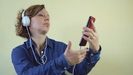 an adult forty-year-old woman in a blue denim shirt in white large headphones holds a mobile phone in her hands. slow motion portrait. beautiful blonde woman