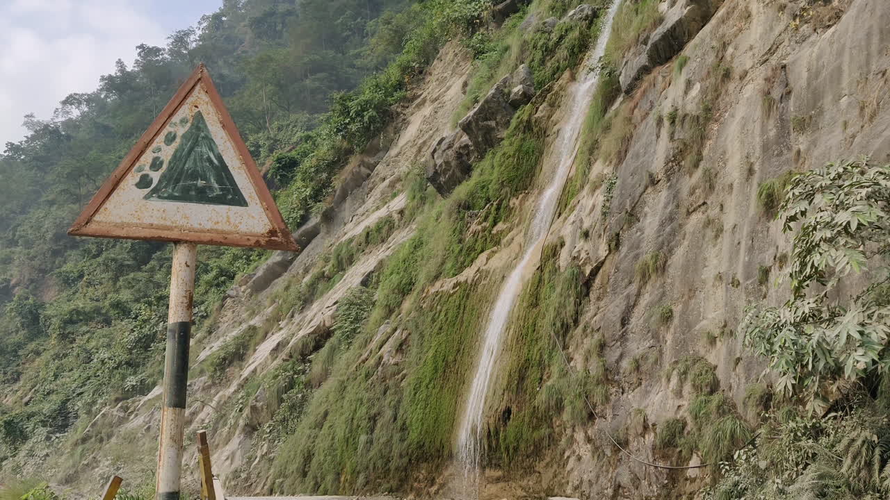 уличный указатель, показывающий оползневую зону и красивый водопад, падающий с гор на заднем плане
