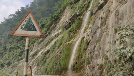 Straßenschild-Mit-Erdrutschgebiet-Und-Einem-Wunderschönen-Wasserfall,-Der-Von-Den-Bergen-Im-Hintergrund-Herunterfällt