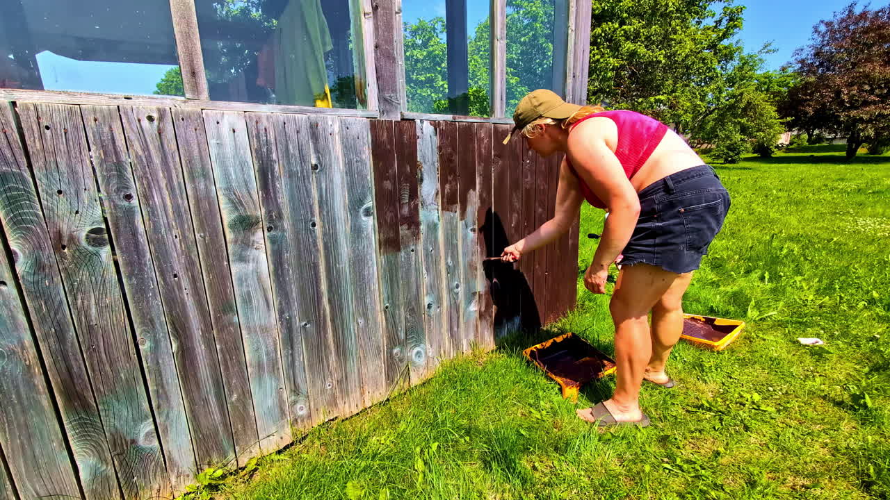 Woman painting weathered wooden wall with children helping in backyard