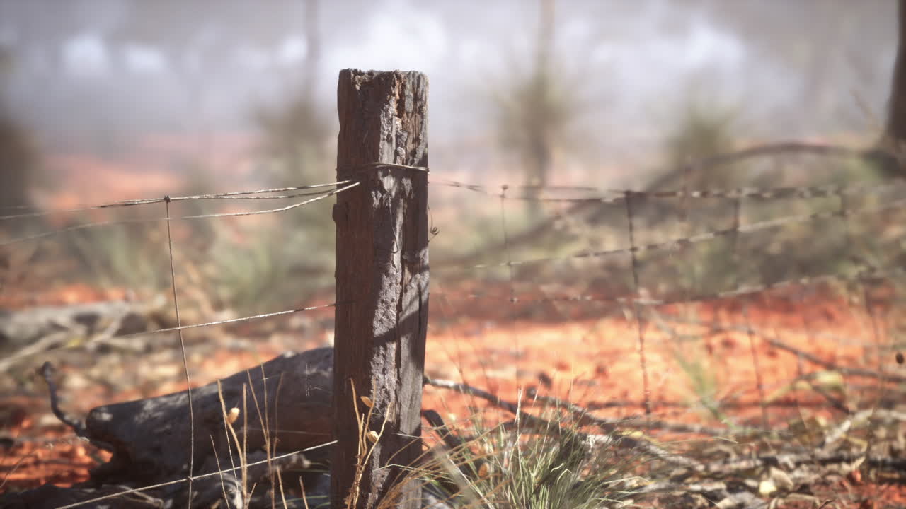 un poste de valla de madera desgastado con alambre de púas en un paisaje de tierra roja en el interior