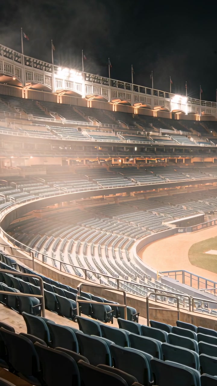 Vertical video: Turning on stadium lights bathing empty curved seats to light stands, haze drifting