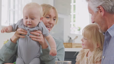 Großeltern-Mit-Erwachsener-Tochter-Und-Enkelkindern-Sitzen-Zu-Hause-Am-Küchentisch