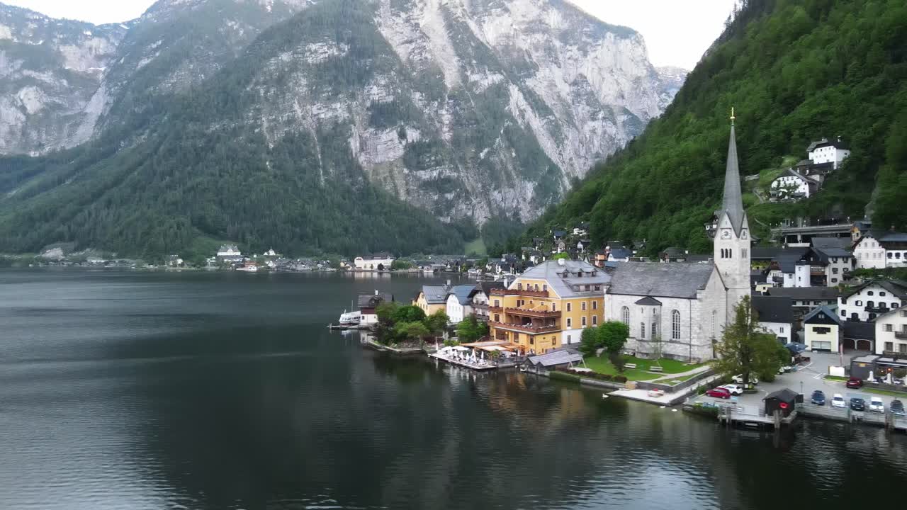 Hallstattin kylä Itävallassa Hallstatt-järvellä Salzkammergutin alppialueella. Ilmakuva ikonisesta kirkosta, järvenrantataloista, tyynestä vedestä ja jyrkistä alppivuorista.