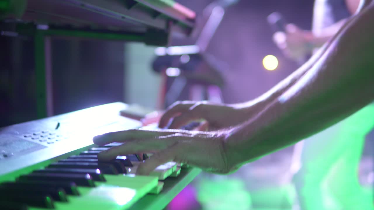 hombre pianista de cerca manos tocando piano eléctrico en un bar nocturno bajo destellos de luces coloridas. toma en cámara lenta