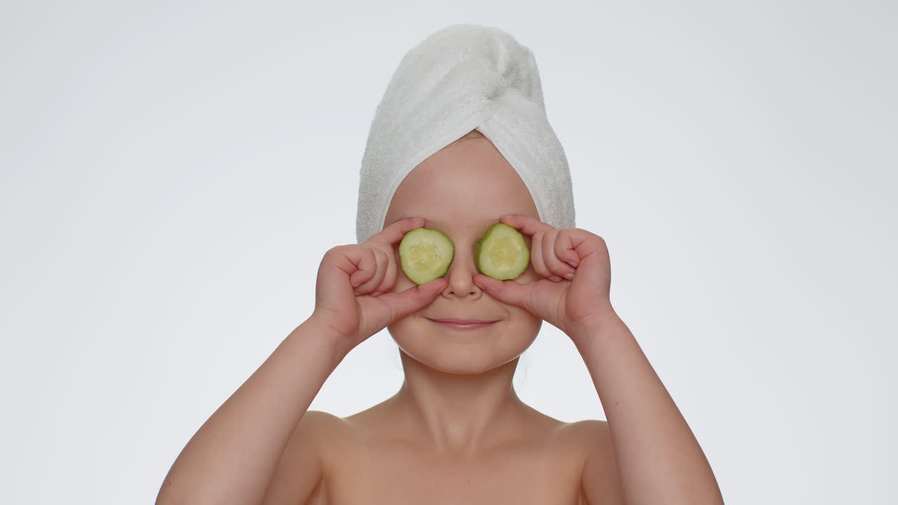 Smiling child girl kid holding slices of cucumber, covering eyes, natural cosmetics, face skin care