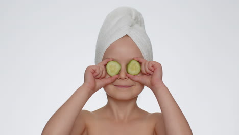 smiling child girl kid holding slices of cucumber, covering eyes, natural cosmetics, face skin care