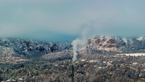 Plume-of-smoke-rises-into-grey-sky-with-snow-covered-Rocky-Mountain-forest-and-stunning-winter-landscape-of-hotel