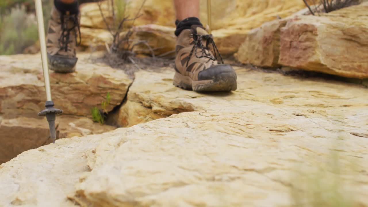 Kaki penyintas pria melintas di medan berbatu dengan sepatu bot pendakian dan menggunakan tongkat pendakian