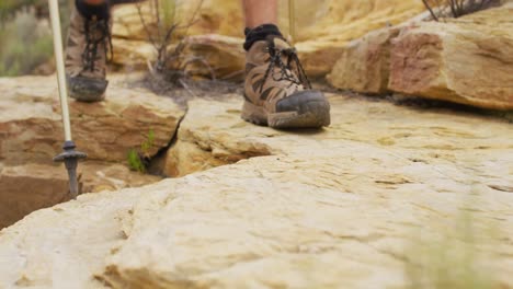 Füße-Eines-Männlichen-Überlebenskünstlers,-Der-In-Wanderstiefeln-Und-Mit-Wanderstöcken-über-Felsiges-Gelände-Wandert