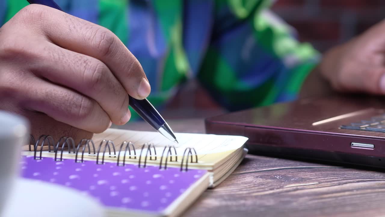 persona que escribe en un cuaderno en el escritorio con una computadora portátil