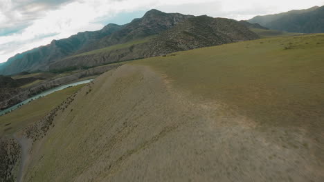 rugged tracks etched along mountain ridge fpv. river valley invites spirit of exploration urging to test limits against wild highland terrain