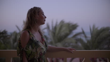 mujer joven en un balcón mirando a lo lejos y disfrutando del viento por la tarde