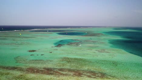 kite surfers gliding over vibrant coral reefs in clear turquoise waters, daytime, aerial view