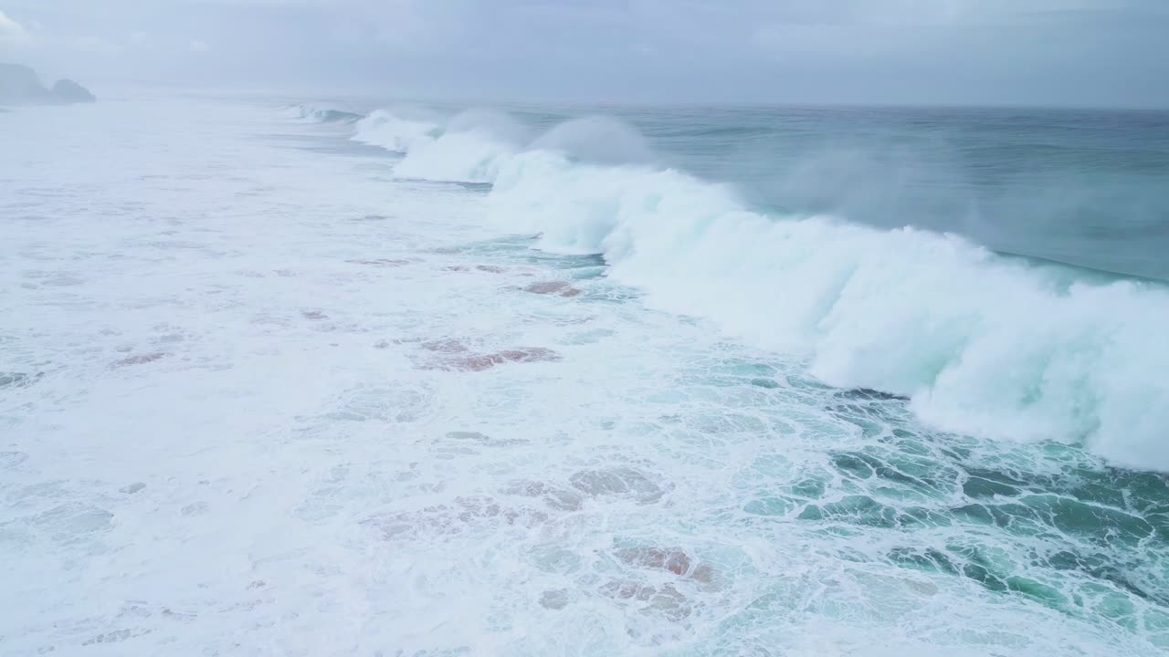 Aerial shot of powerful ocean waves crashing onto the sandy shore in slow motion