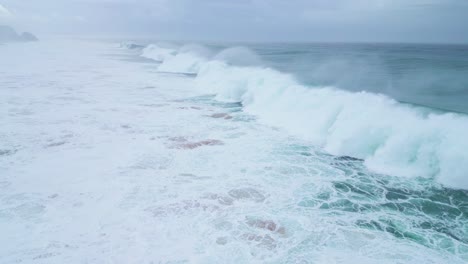 aerial shot of powerful ocean waves crashing onto the sandy shore in slow motion