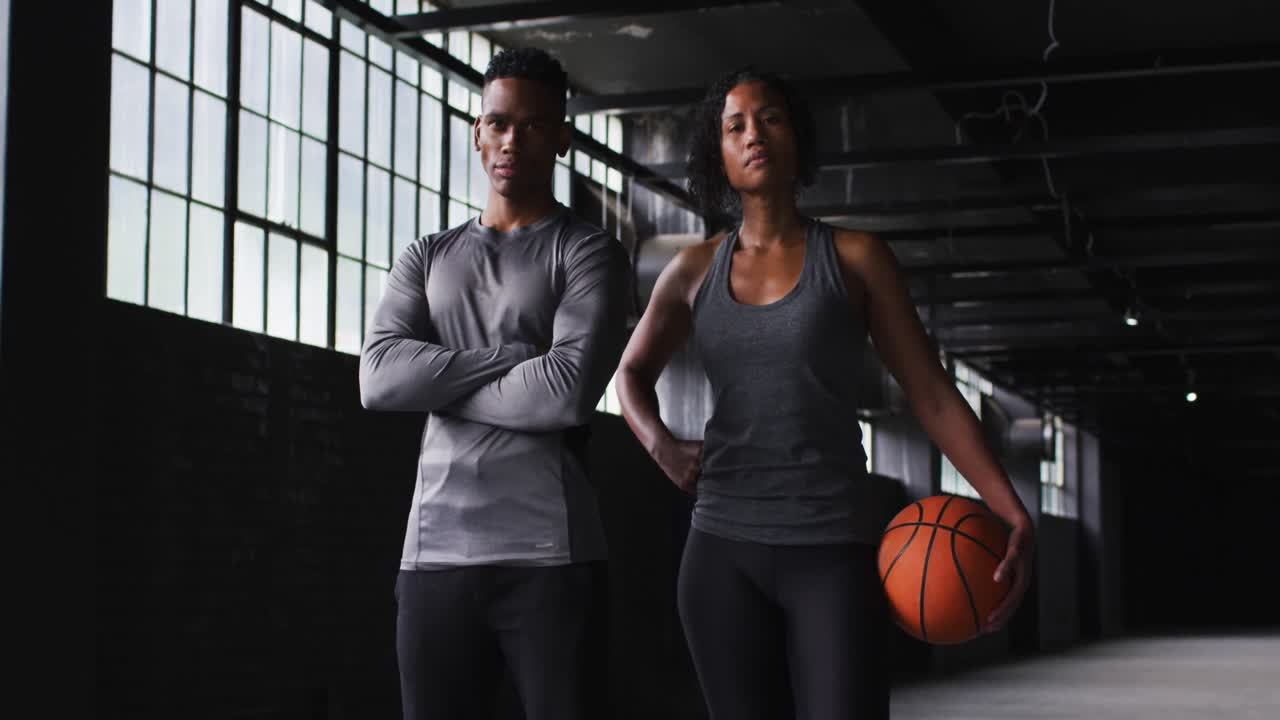 African american man and woman standing in an empty building holding a basketball