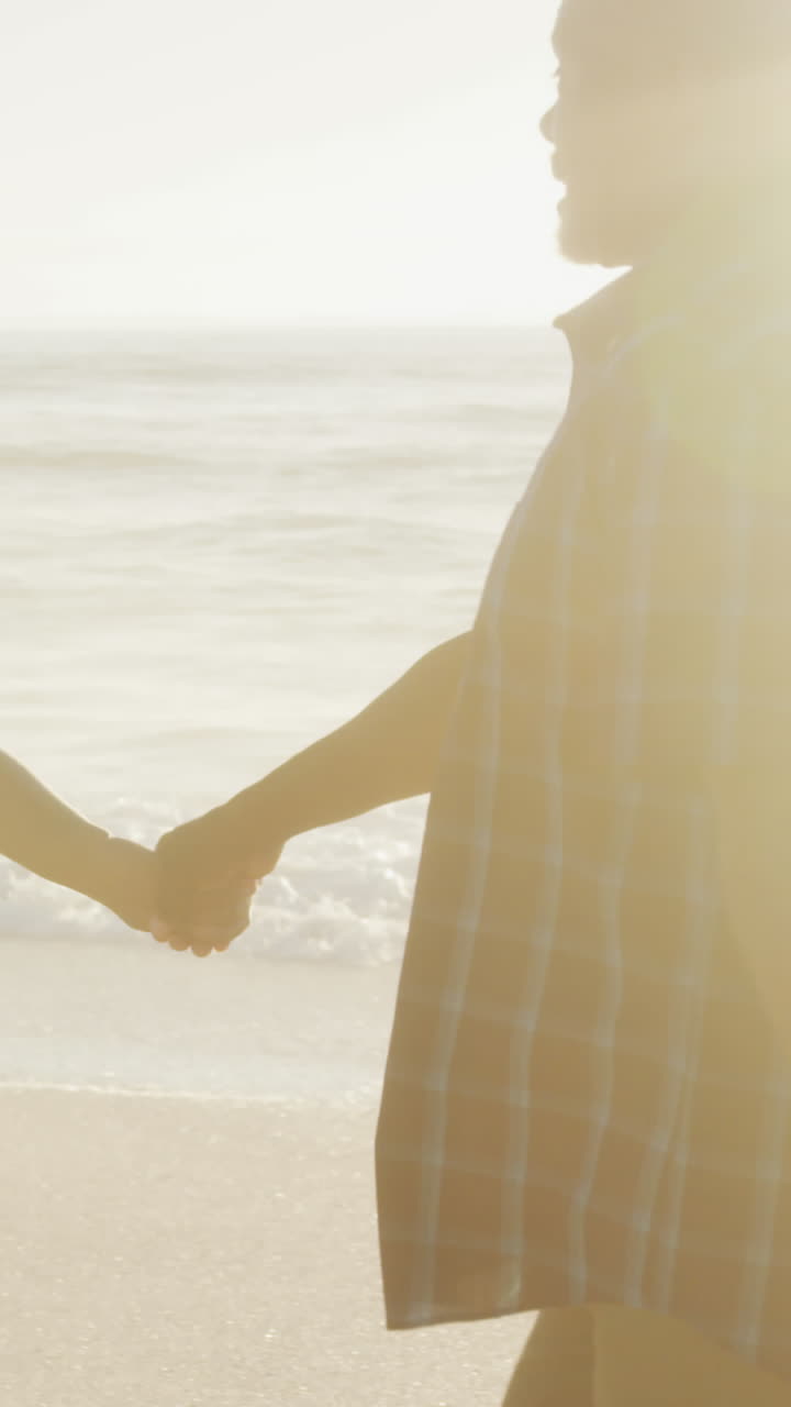 웃는 아프리카계 미국인 부부가 손을 잡고  ⁇ 은 해변에서  ⁇ 고 있습니다.