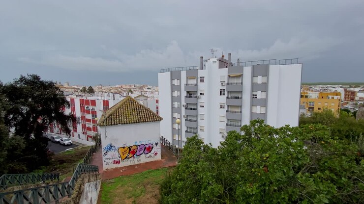 Vista panorâmica de uma vibrante praça de touros cercada por árvores e casas baixas sob pesadas nuvens de tempestade
