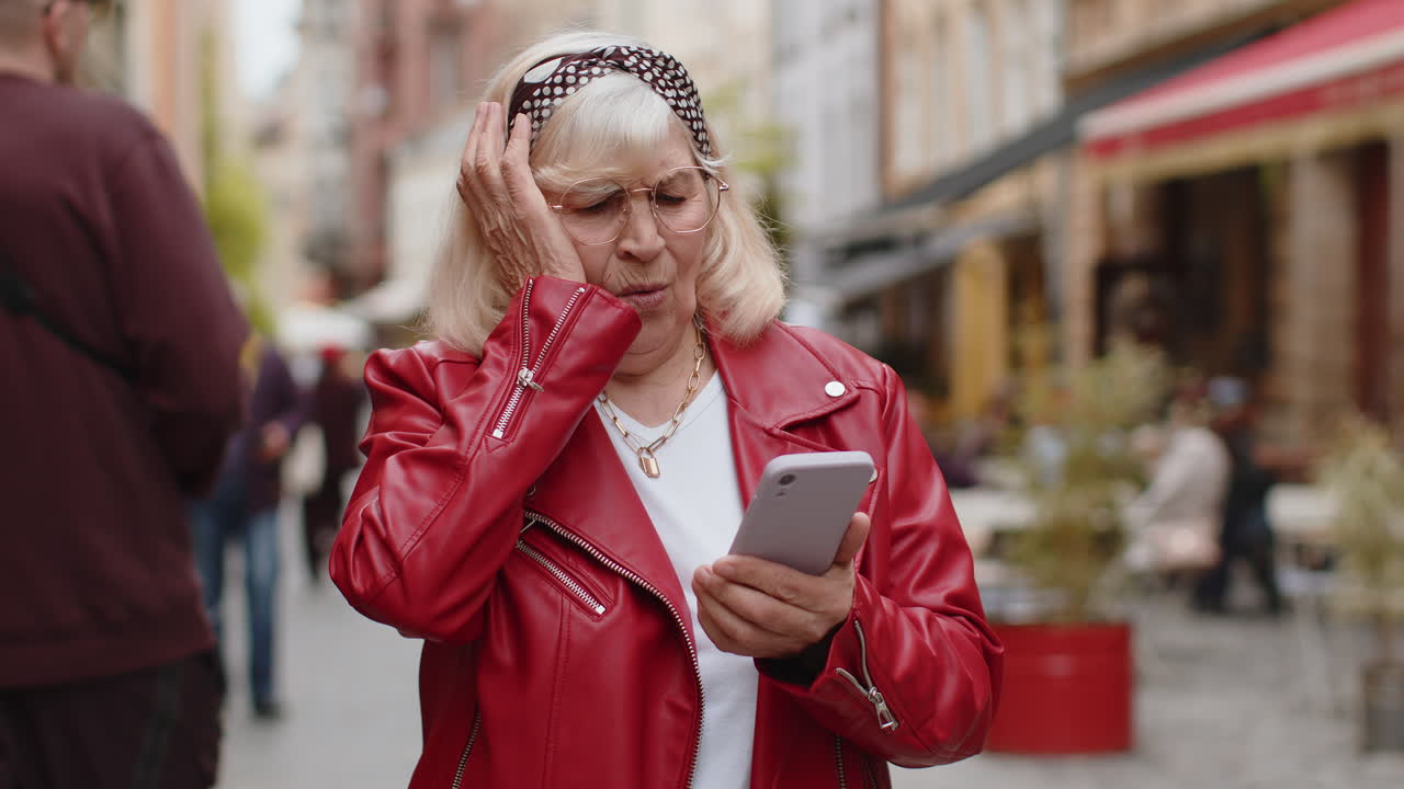 Surprised senior woman use smartphone loses bad news fortune loss fail outdoors in city street