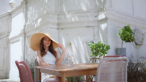 rich girl looking camera sitting summer patio. lady in trendy straw hat posing