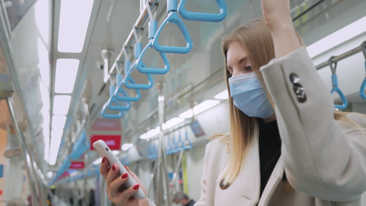 Woman using smartphone in a subway train wearing a face mask