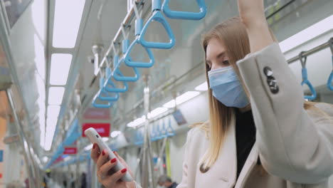woman using smartphone in a subway train wearing a face mask