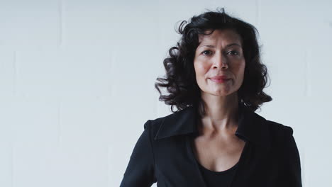 Portrait-Of-Determined-Mature-Businesswoman-In-Suit-Standing-Against-White-Studio-Wall