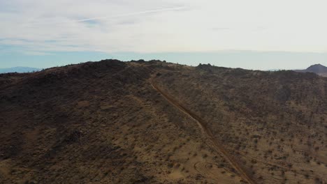 Vehículo-Todo-Terreno-Subiendo-Una-Pendiente-Empinada-Hasta-La-Cima-Para-Revelar-El-Vasto-Paisaje-Del-Desierto-De-Mojave---Vista-Aérea