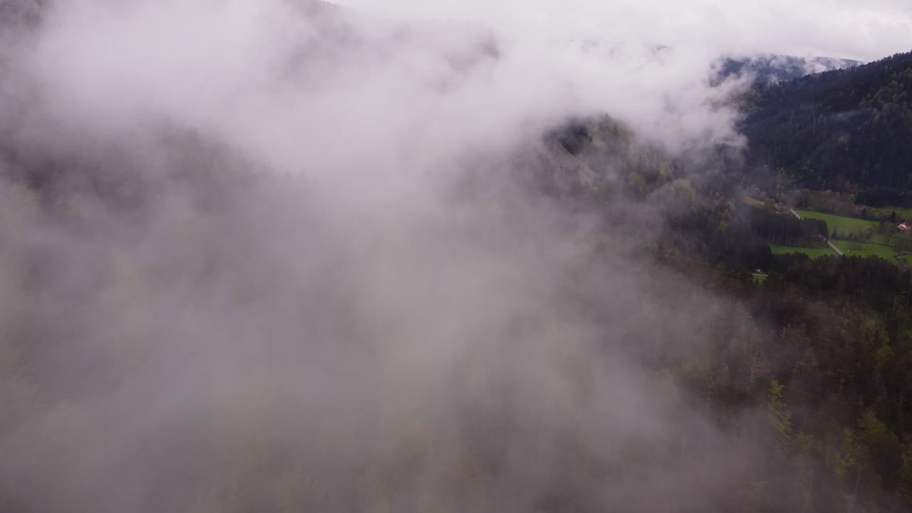 Drone slow fly through white clouds over a moody forest mountain valley during spring time