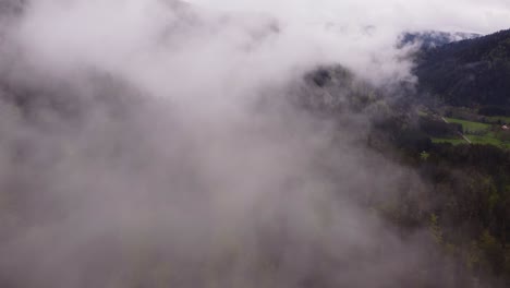 drone slow fly through white clouds over a moody forest mountain valley during spring time