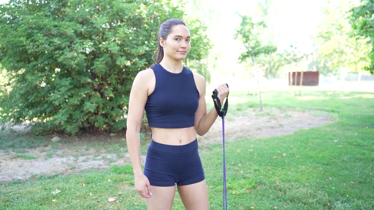 Una donna in abbigliamento sportivo blu svolge allenamento fitness all'aperto con una fascia di resistenza nel verde.