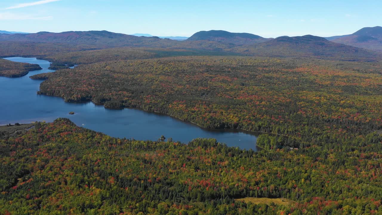un dron aéreo se inclinó hacia abajo sobre un sereno lago azul de montaña en el bosque a lo largo de una cordillera cuando termina el verano y la temporada cambia para caer en maine
