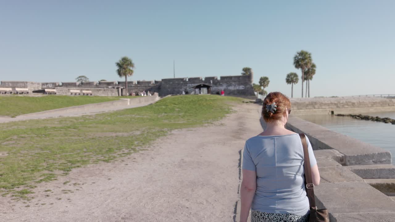 Middle aged caucasian woman walking on a spring day near Castillo de San Marcos National Monument in St. Augustine, Florida with gimbal video walking behind in slow motion