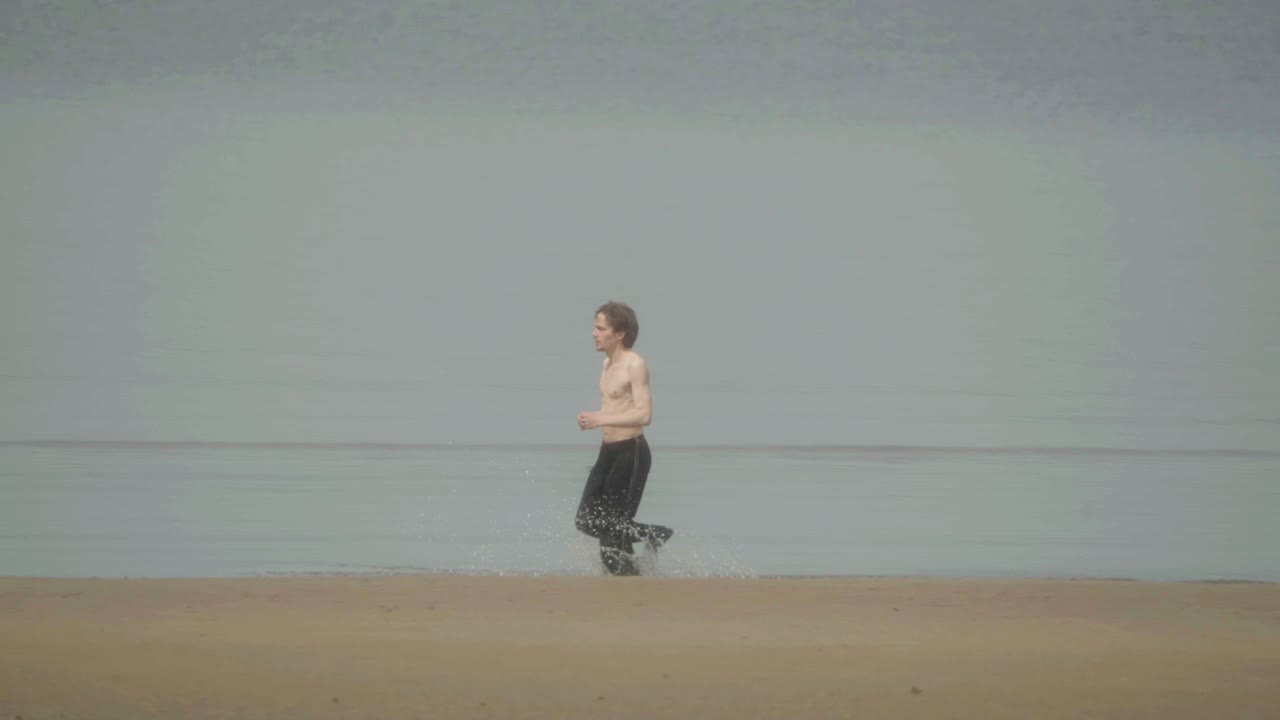 hombre adulto sin camisa corriendo en el agua en la orilla del mar, cámara lenta