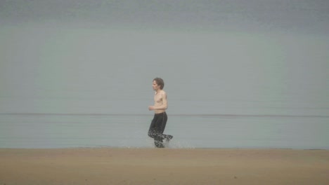 Adult-male-shirtless-running-in-water-at-edge-of-the-sea,-slow-motion