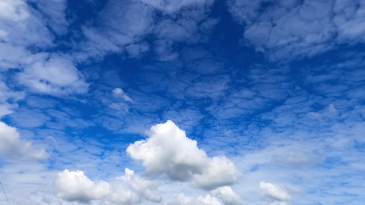 Cirrocumulus clouds gathering in the sky. Some cumulus clouds float lower. Atmospheric phenomena low angle view. Timelapse.