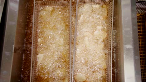 Potato-dippers-deep-fried-in-oil-in-baskets-in-kitchen,-overhead-shot