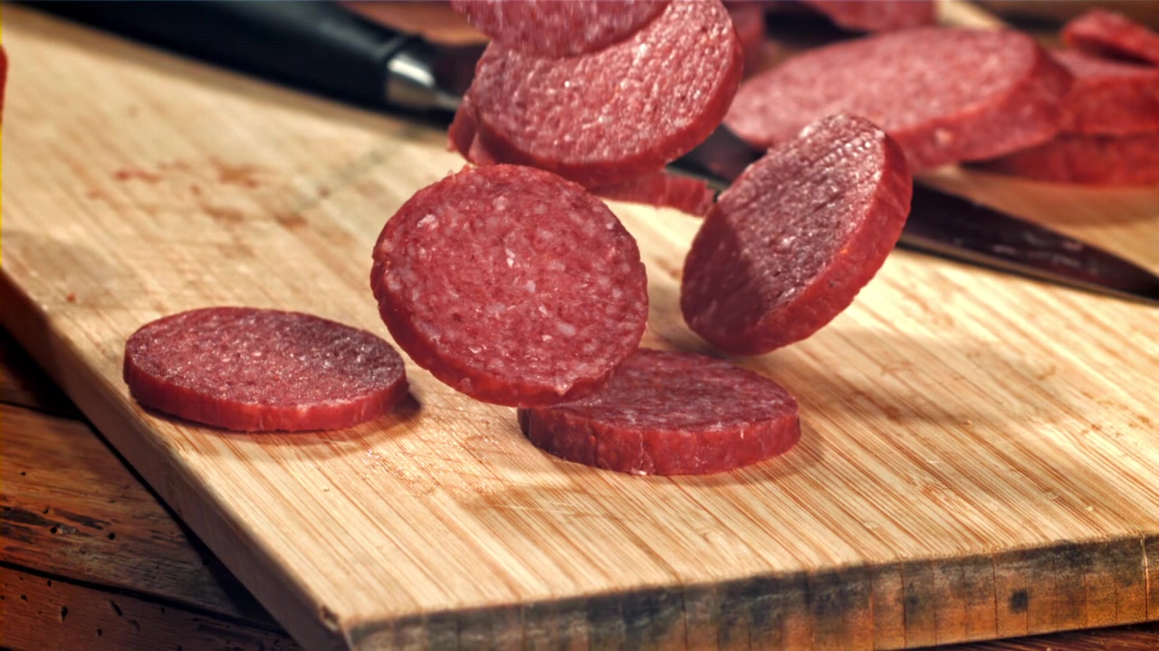 Fette di salame al rallentatore che cadono su un tagliere di legno