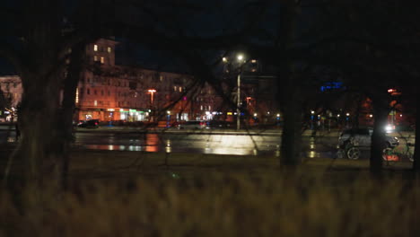 close view of an urban street at night with illuminated buildings and street lights, with car passing on the road